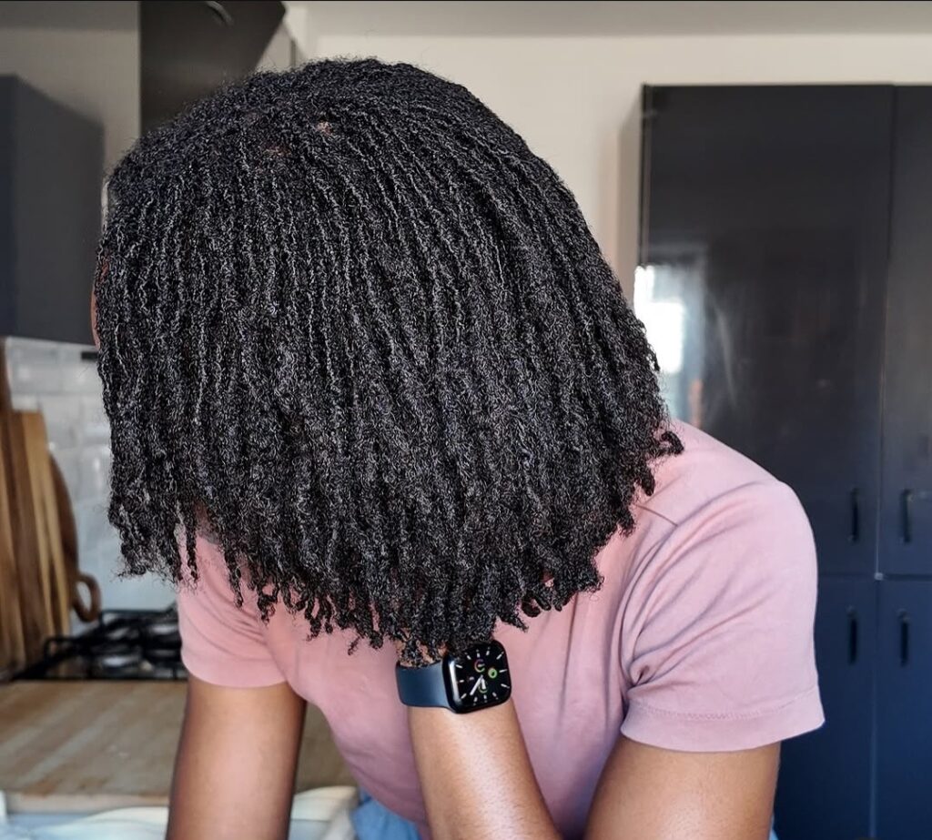 Side view of a woman’s full medium-length locs with neat parting, dark roots
