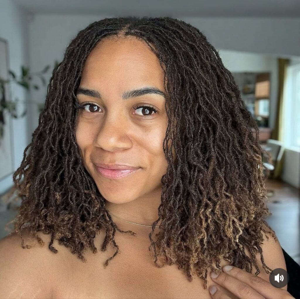 Woman smiling at a picture with long brown and black locs touching her shoulders.