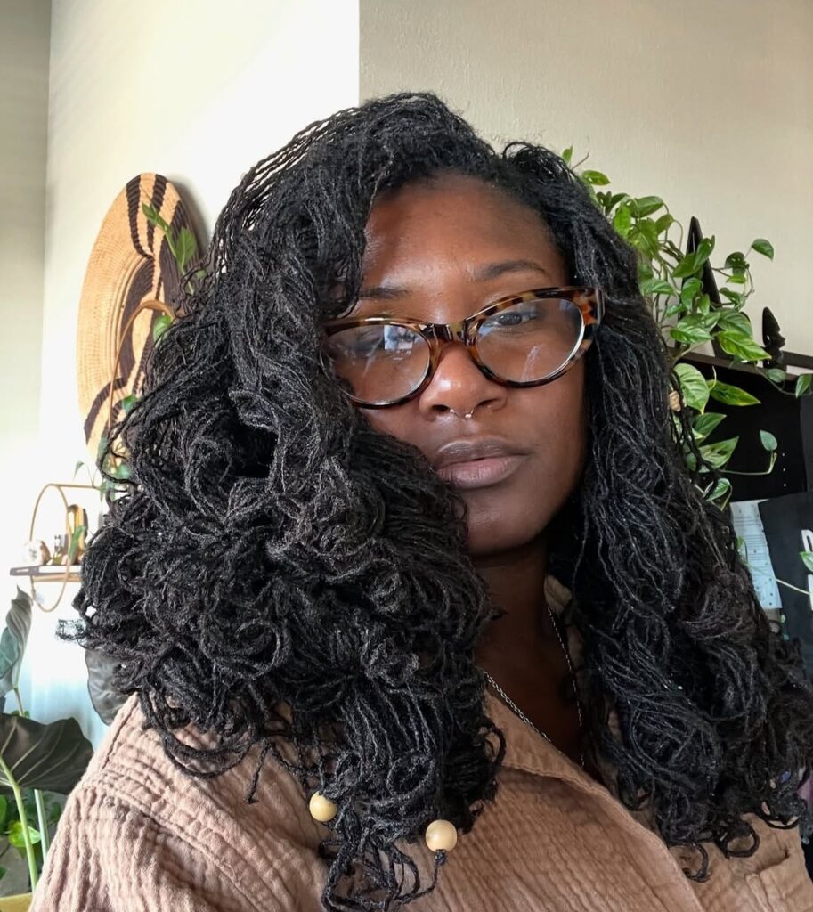 Woman with long, soft curly locs styled down, showing mature loc texture and volume.
