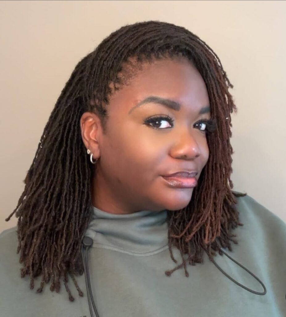 Woman wearing shoulder-length brown and black locs styled in two high pony buns with loose locs framing the face.