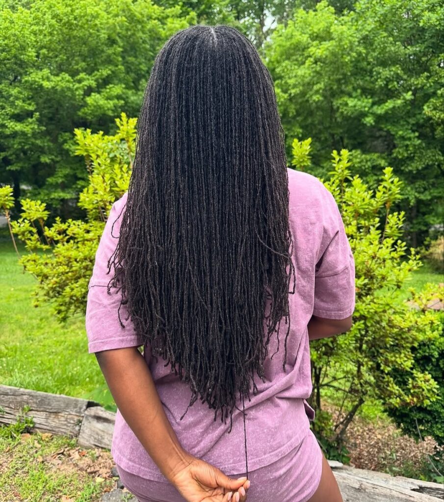 Woman standing outside on a sunny spring day, turned back, showing long, full locs.