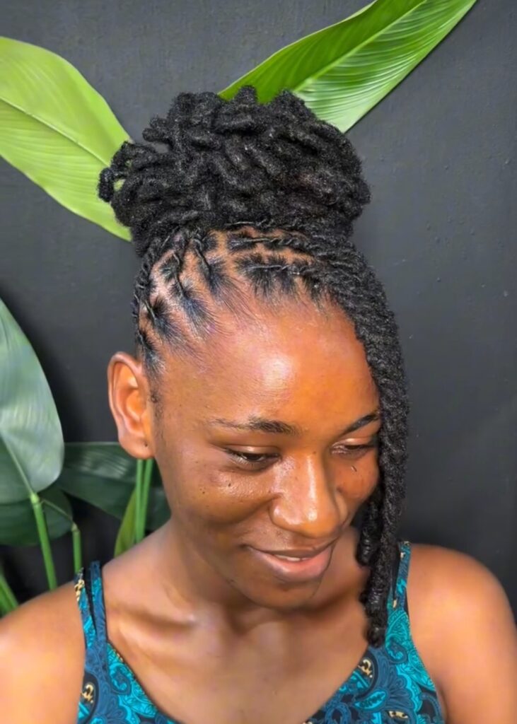Woman smiling with neatly styled locs in an updo, featuring clean cornrowed roots and a side loc.